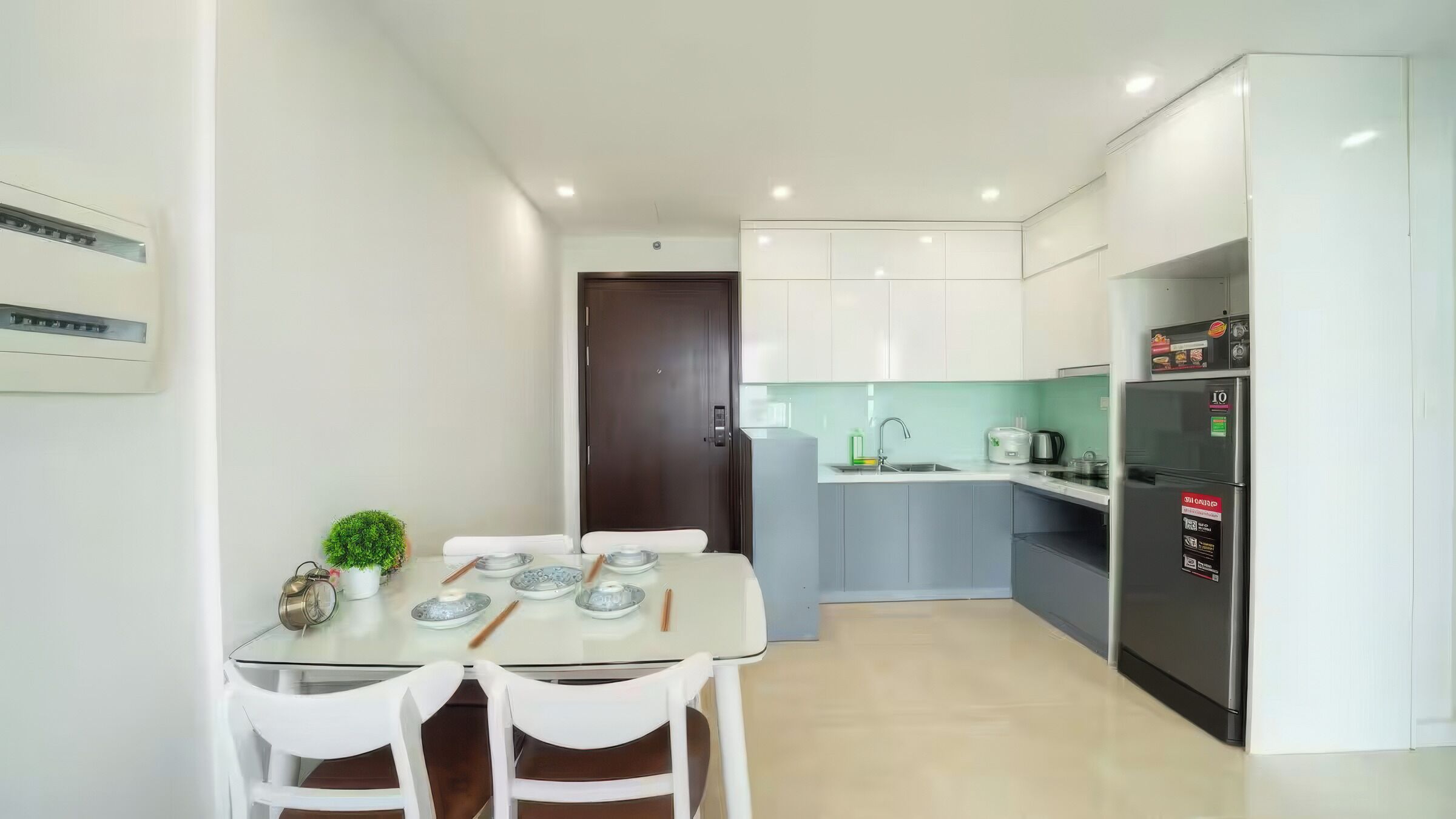 A modern kitchen with white cabinets, a stainless steel refrigerator, and a dining area with a table and chairs.
