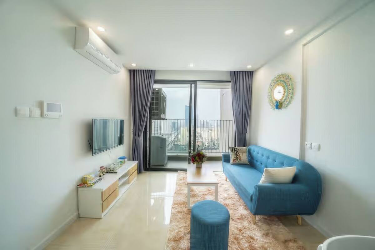 A modern living room with a blue sofa, a flat-screen TV, and a large window with curtains.