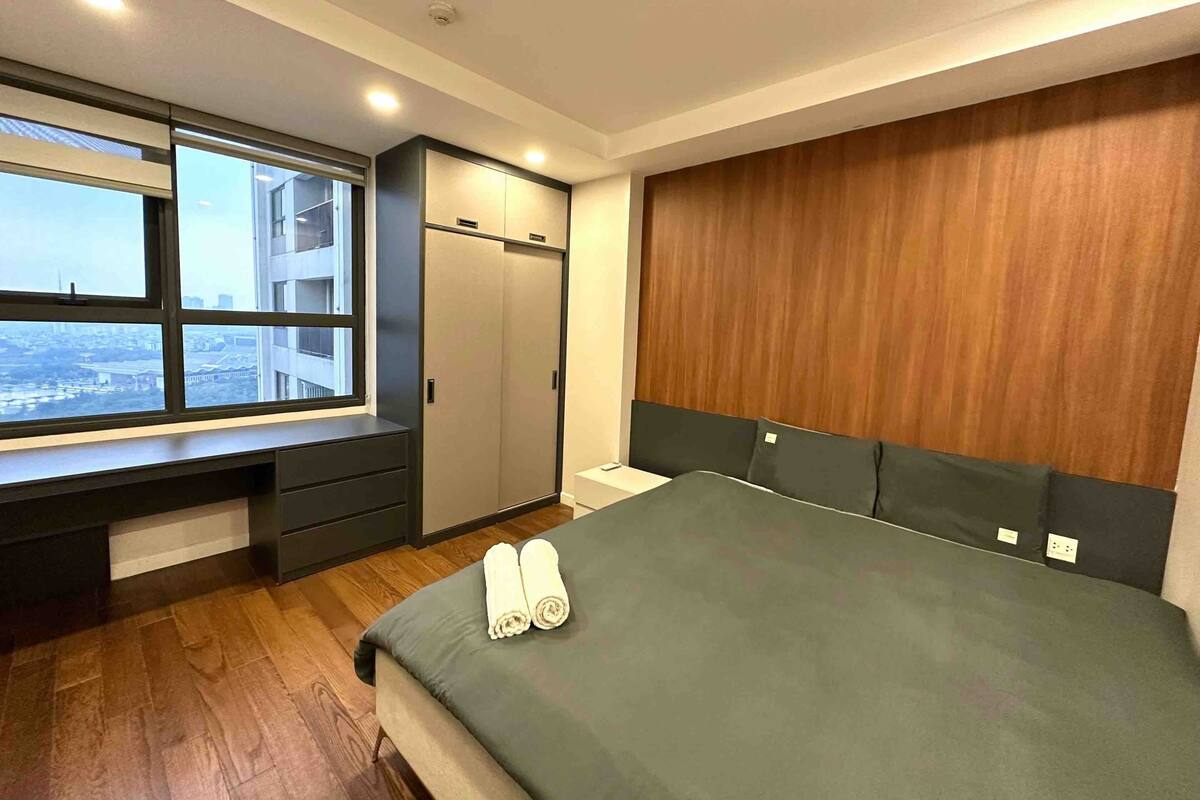A modern bedroom with a large bed, a desk, and a wardrobe.