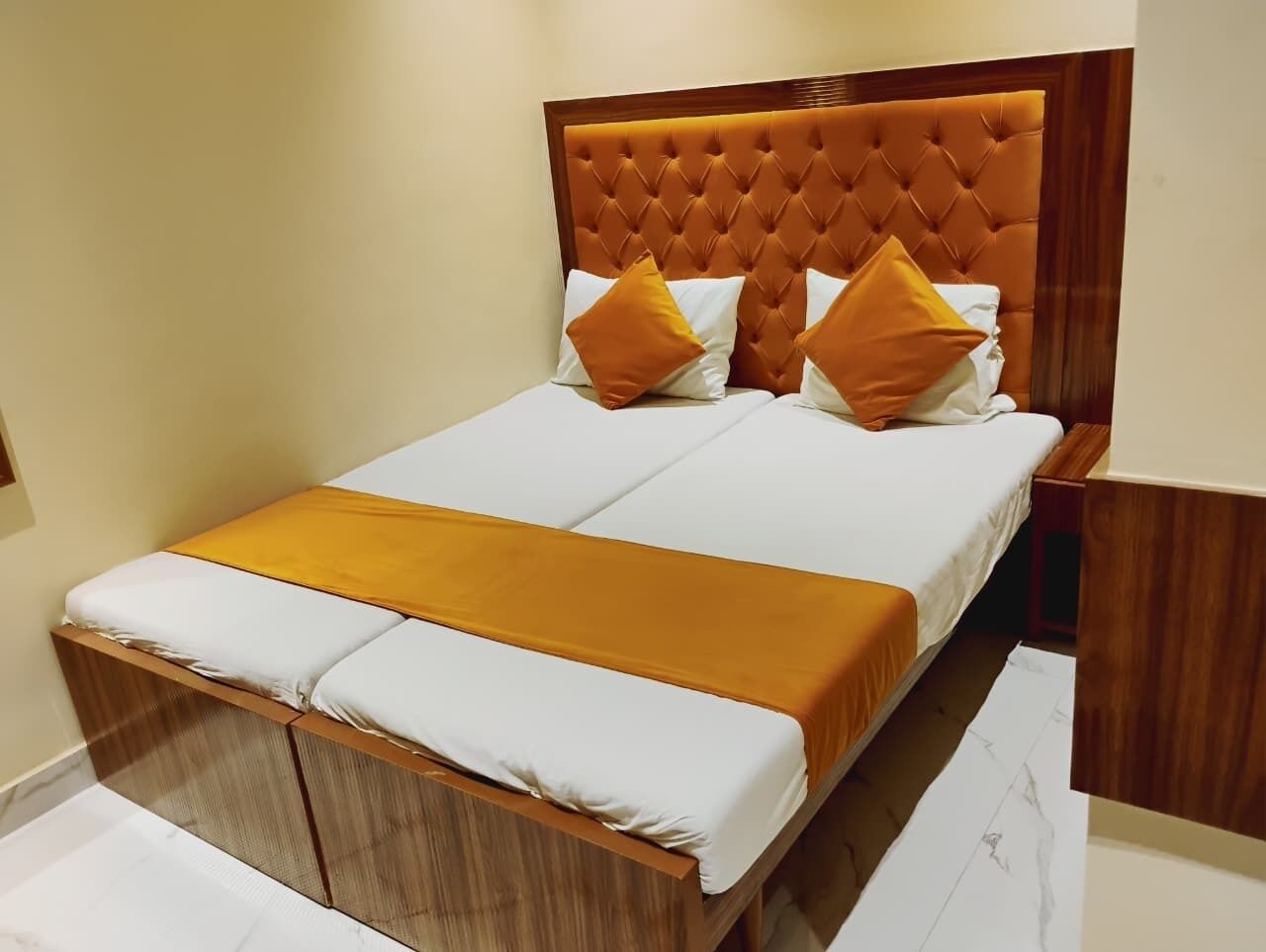 A double bed with a wooden frame, white bedding, and two orange pillows.
