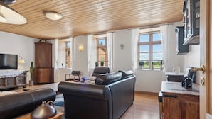 Ein Wohnzimmer mit einer Couch, einem Holztisch, einem Fernseher und Fenstern mit Vorhängen.