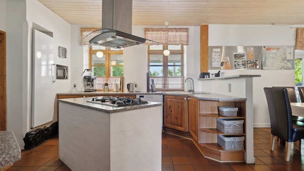 Eine moderne Küche mit einer zentralen Kochinsel, Holzschränken, einem Edelstahlkühlschrank und einem Fenster mit Aussicht.