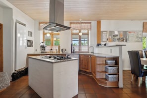 A modern kitchen with a central island, wooden cabinets, a stainless steel refrigerator, and a window with a view.