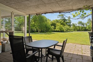 An outdoor patio with a table and chairs, a covered area with a view of a grassy field and trees. - Large holiday home near Tønder (Tønder)