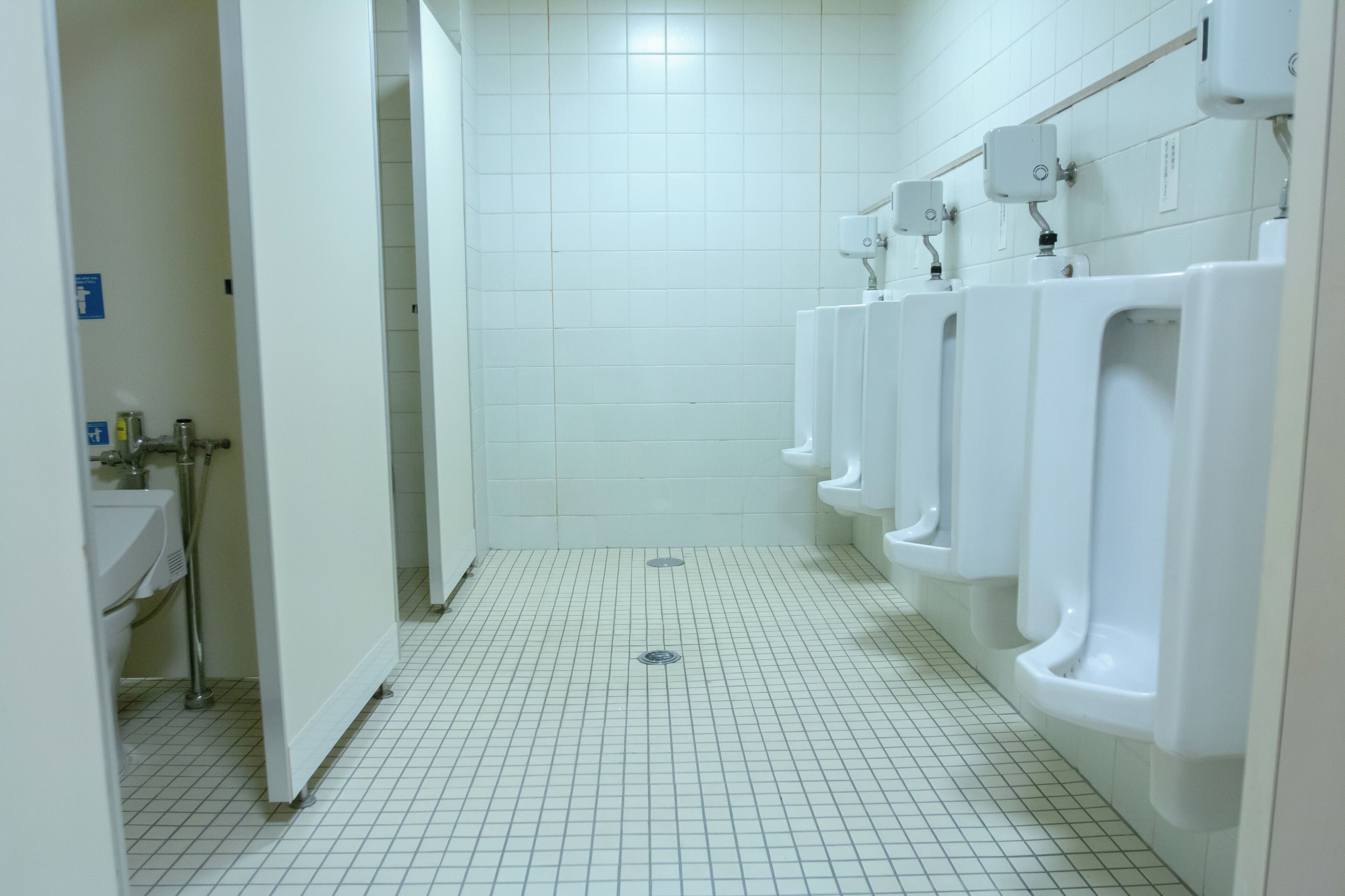 A public restroom with multiple urinals, a sink, and a tiled floor.