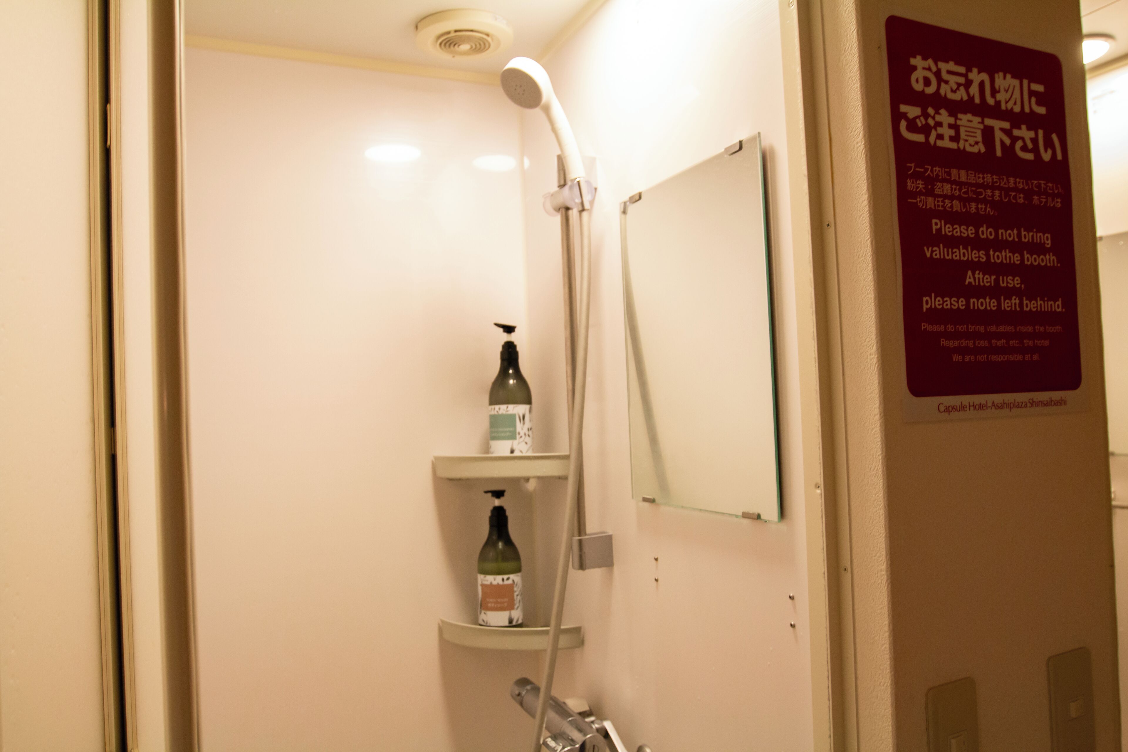 Casa de banho de hotel com chuveiro, espelho e um aviso em japonês.