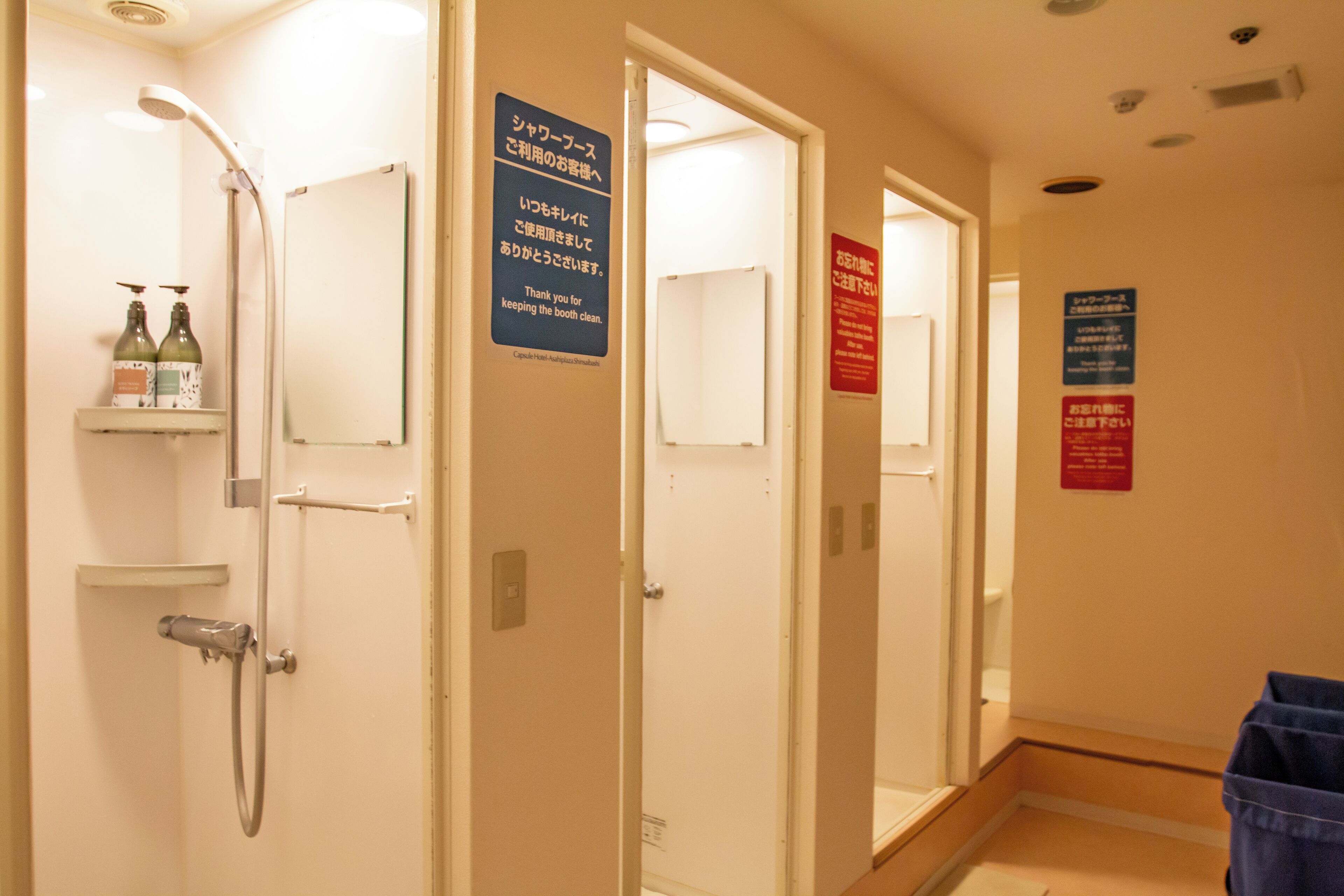 A hotel bathroom with a shower, a sink, and a mirror. There are signs on the walls and a shelf with toiletries.