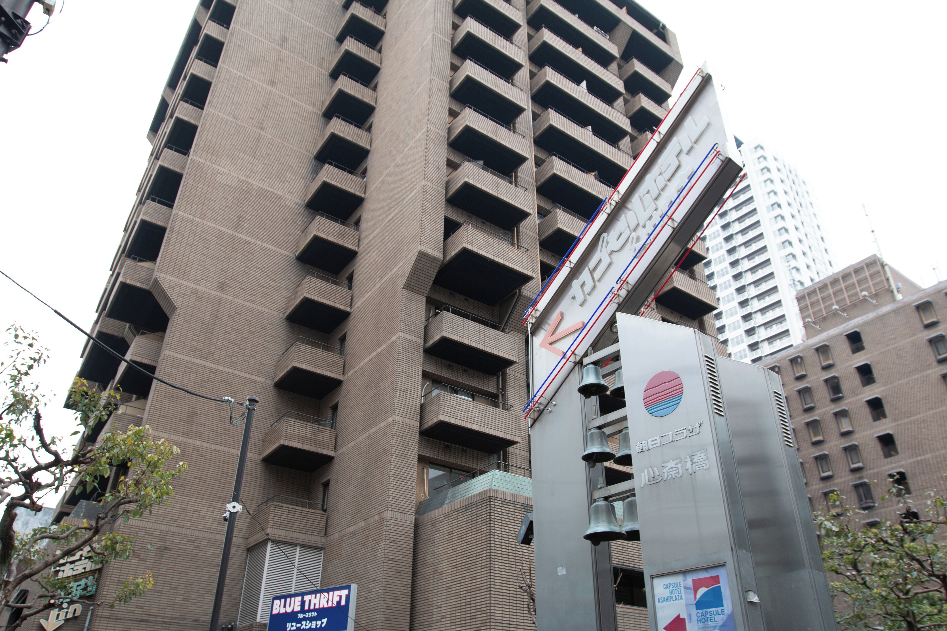 A tall building with multiple balconies and a sign for 'Blue Thrift' on the ground floor.
