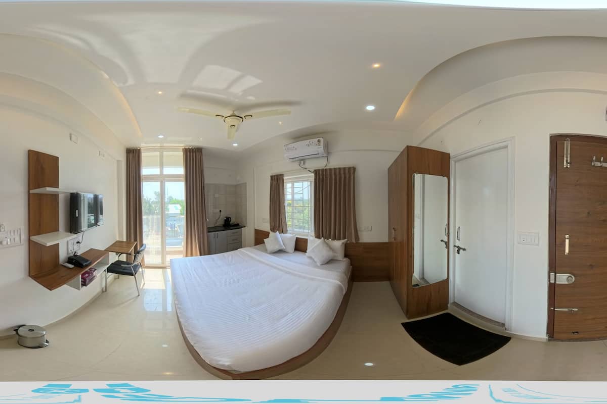 A modern hotel room with a large bed, a desk with a chair, a wardrobe, and a TV.