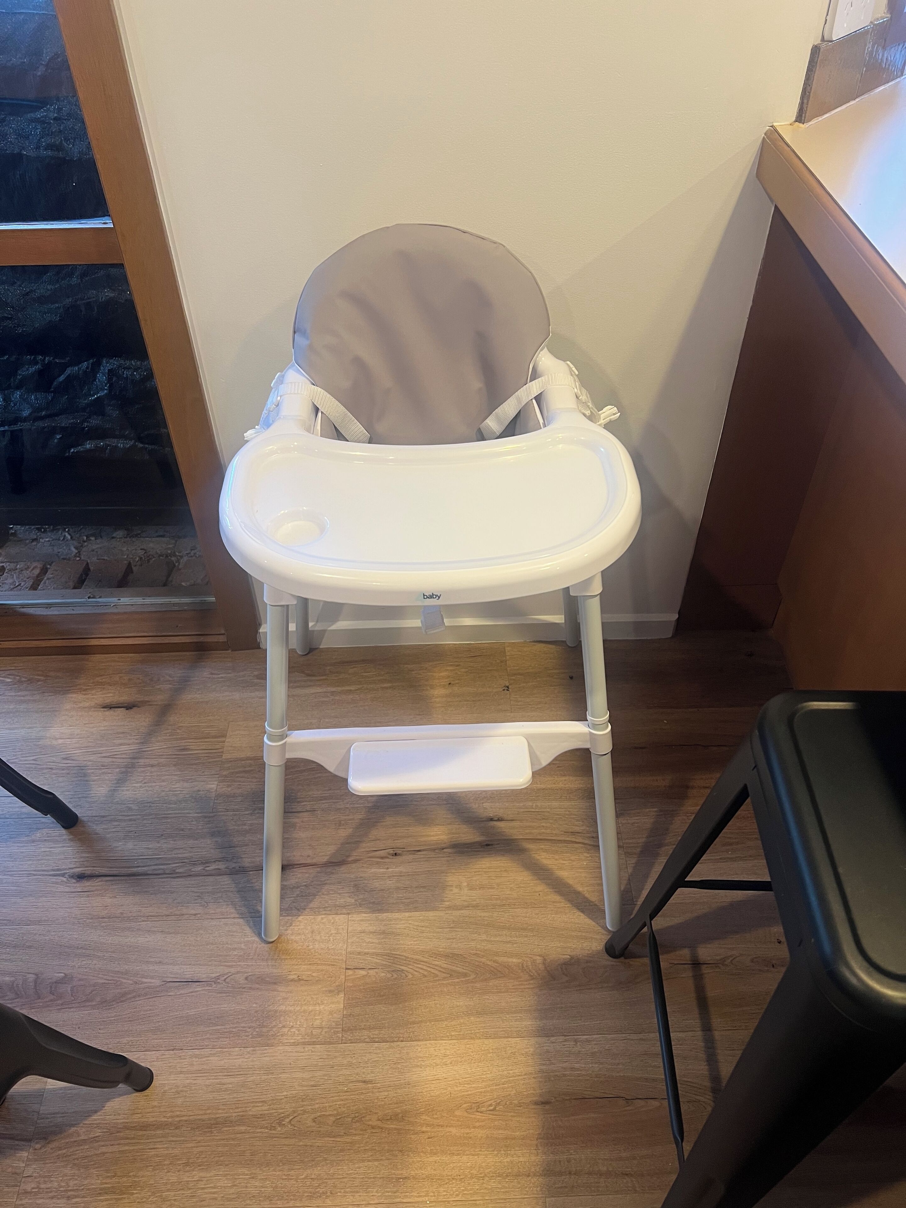 Ein weißer Babyhochstuhl mit Tablett, auf einem Holzboden vor einer Wand platziert.