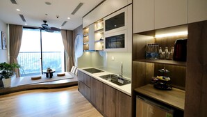A modern kitchen with a built-in oven, a sink, and a refrigerator. There is a window with curtains and a plant on the left side. - Onsen Landmark Luxury Apartments (Phung Cong)