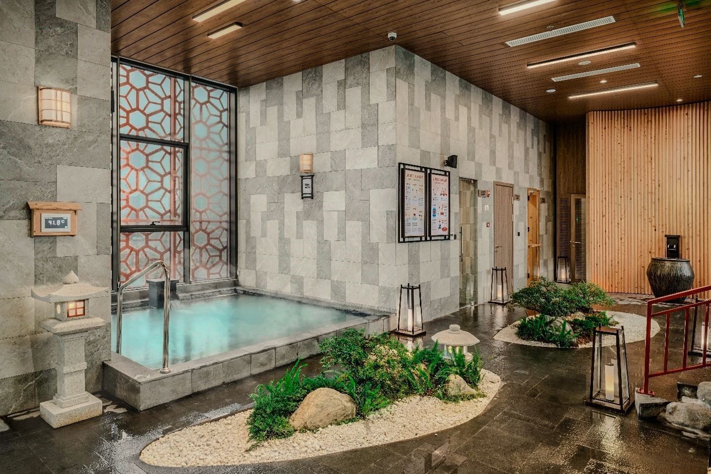 A spa area with a hot tub, stone walls, wooden ceiling, and a small garden with plants and rocks.