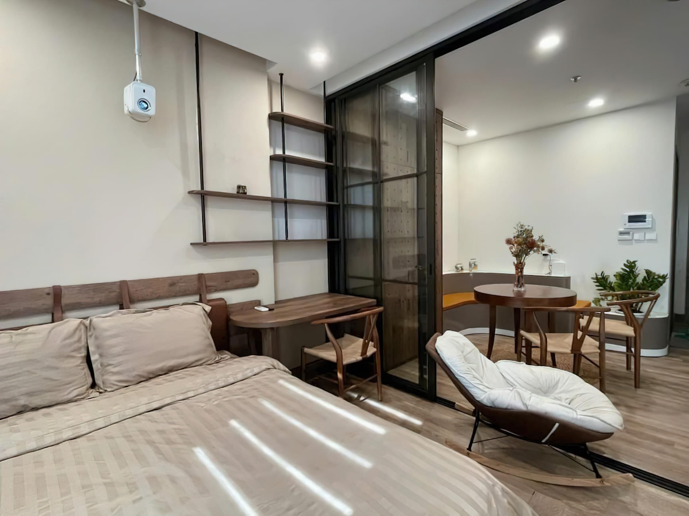 A modern hotel room with a bed, a desk, a chair, and a small dining area.