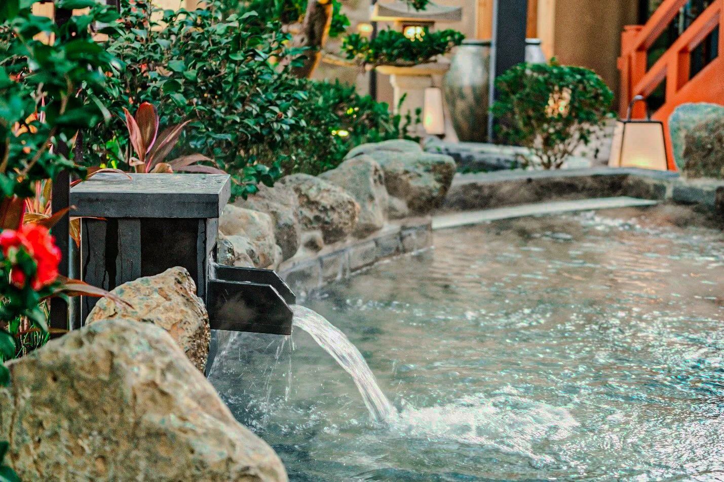 A water feature with a stone structure and a small waterfall, surrounded by greenery and rocks.