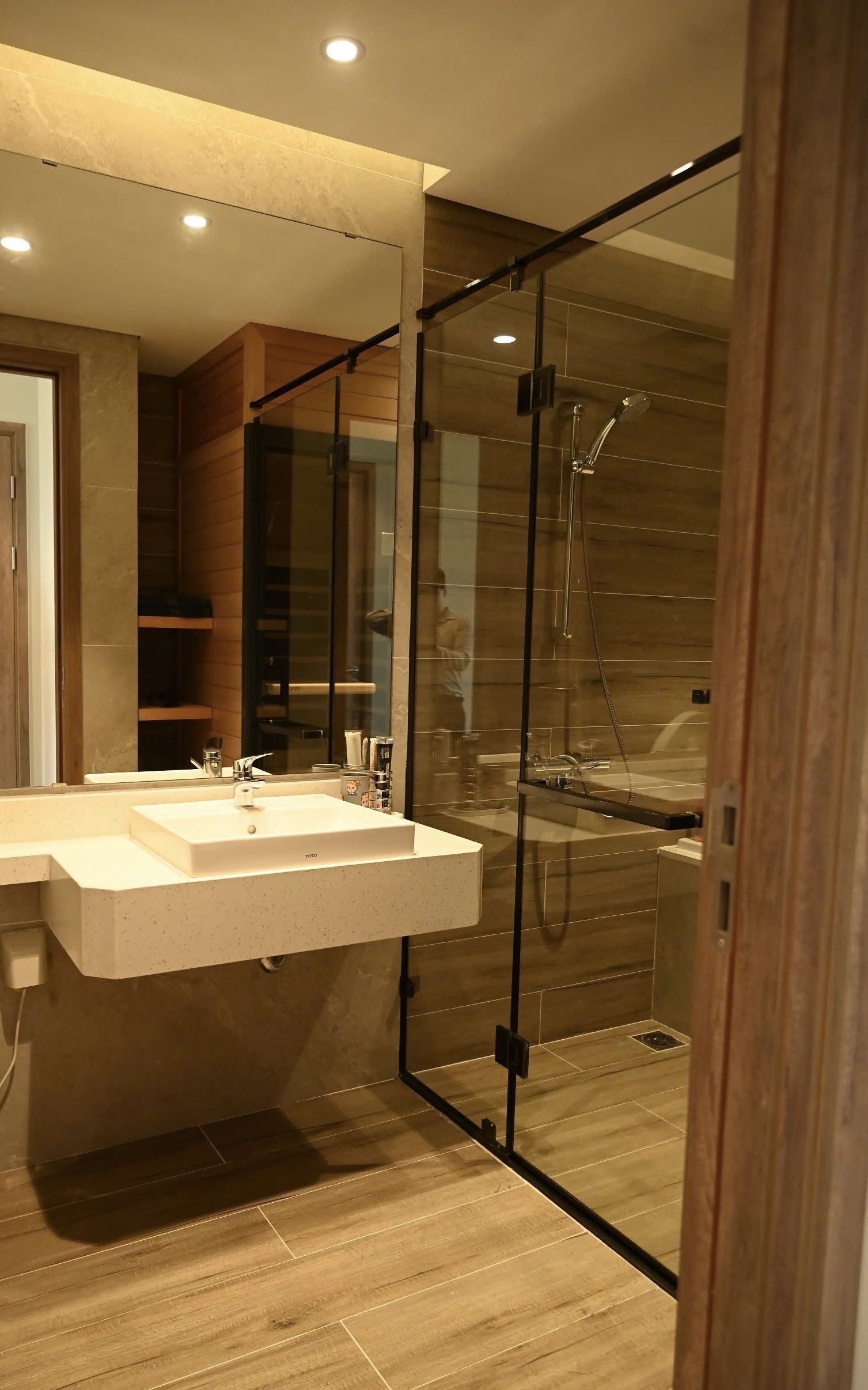 Un baño moderno con cabina de ducha de vidrio, un espejo grande y suelo de madera.