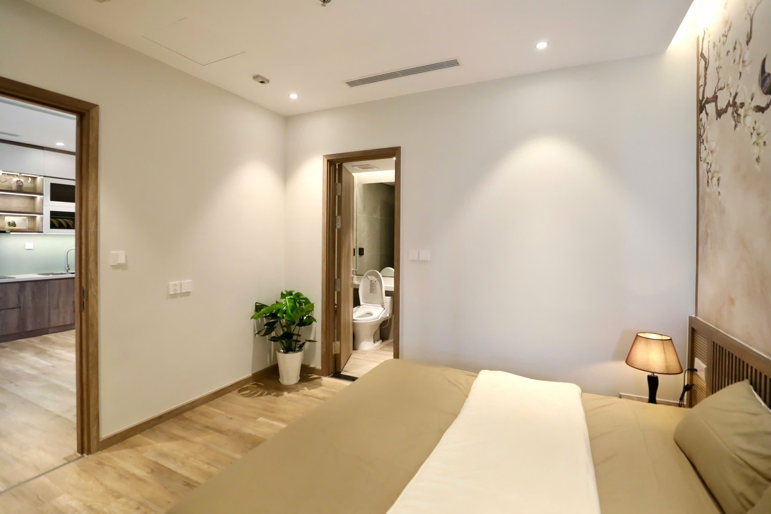 Una camera d'albergo con un letto, una lampada da comodino, una pianta in vaso e vista sul bagno.
