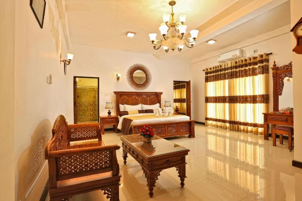 A spacious bedroom with a large bed, a wooden nightstand, a bedside table, a chandelier, and a window with curtains.