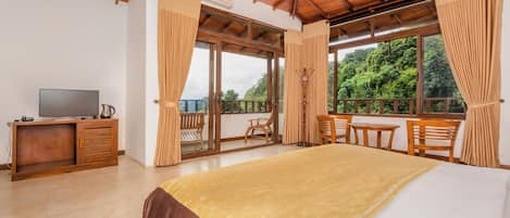 Un dormitorio con una cama grande, muebles de madera, un televisor y un balcón con vistas a zonas verdes.