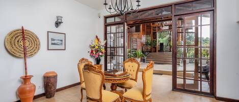 Uma área de refeições com uma mesa redonda e quatro cadeiras, um candelabro e uma grande porta de vidro deslizante que dá para um espaço ao ar livre.