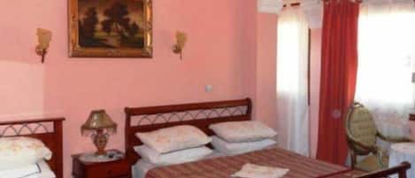 A bedroom with two beds, a painting on the wall, and a window with curtains.