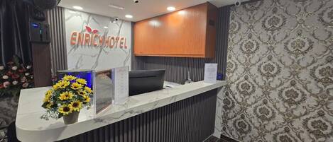A hotel reception desk with a marble counter, a laptop, and a floral arrangement.