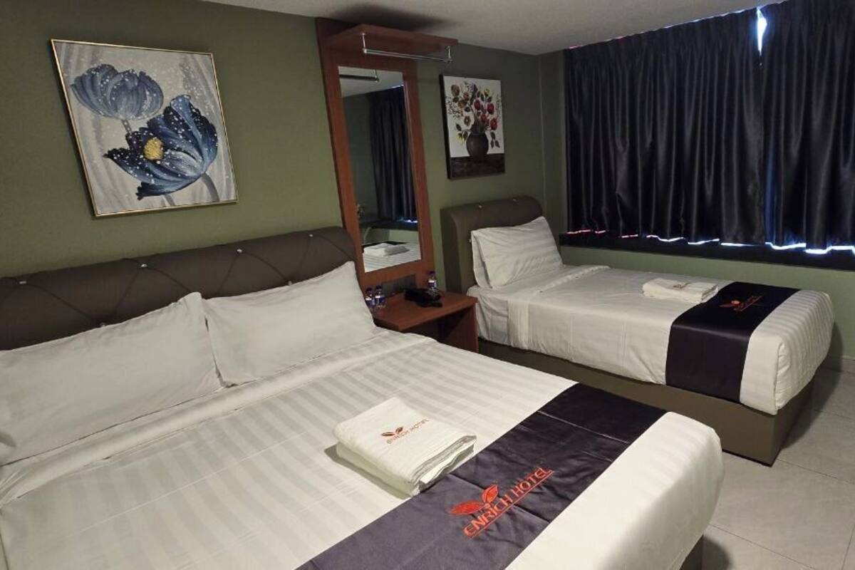 Ein Hotelzimmer mit zwei Betten, einem Nachttisch, einem Spiegel, einem Fenster mit Vorhängen und einer Wand mit einem Blumenbild.