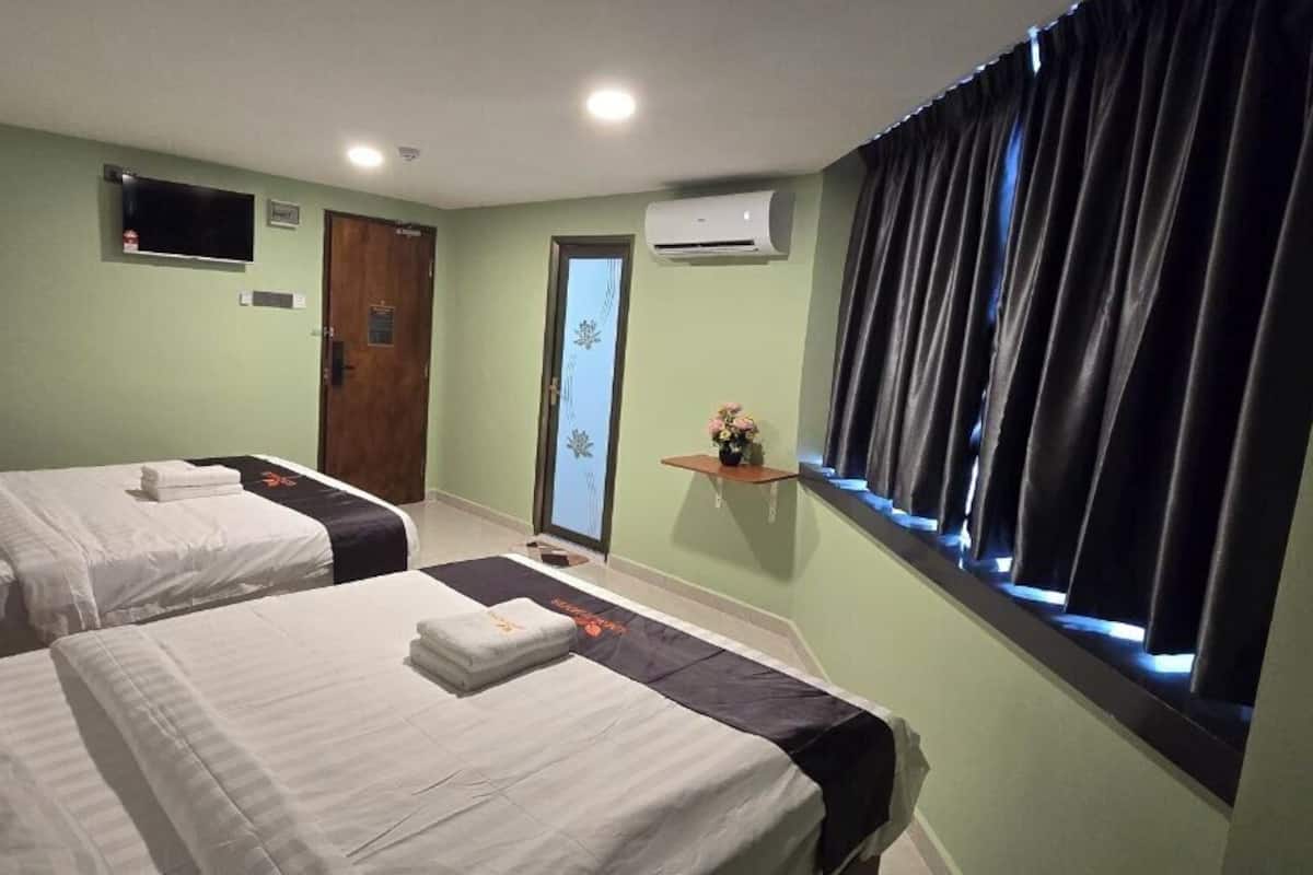 Ein Hotelzimmer mit zwei Betten, einem Fernseher, einer Klimaanlage, einem kleinen Fenster mit Vorhängen und einer Tür.
