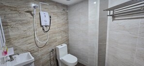 Kylpyhuone, jossa on marmoriseinä, valkoinen wc-istuin, pesuallas ja käsisuihkusuutin.