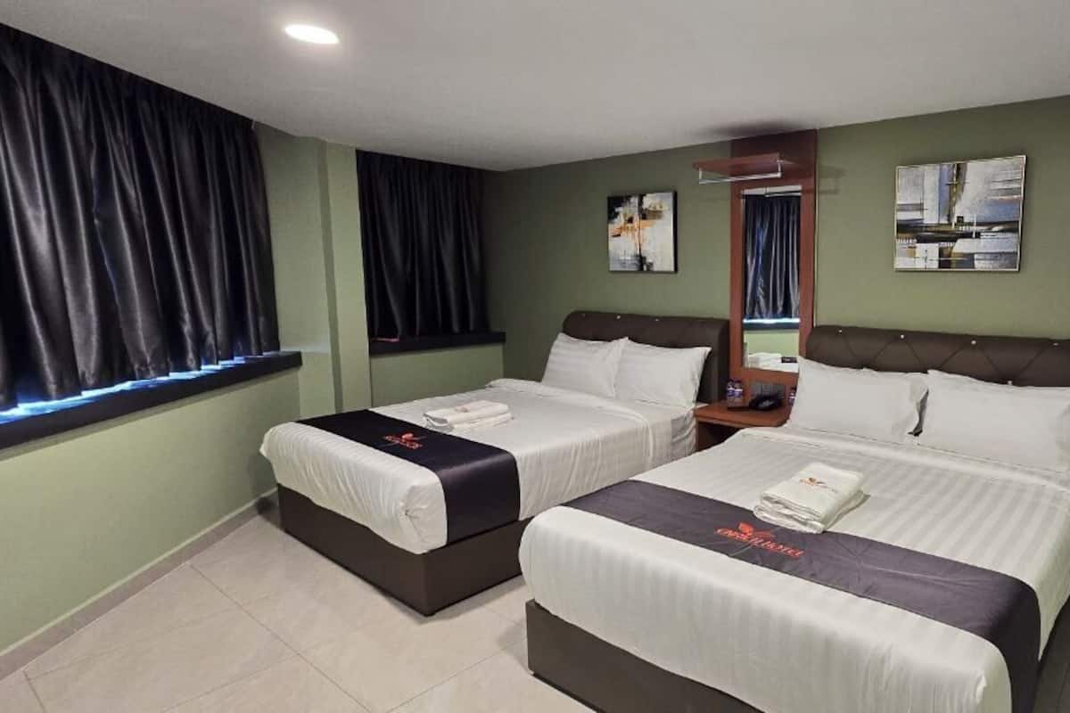 Ein Hotelzimmer mit zwei Einzelbetten, einem kleinen Tisch, einem Fernseher und einem Fenster mit Vorhängen.