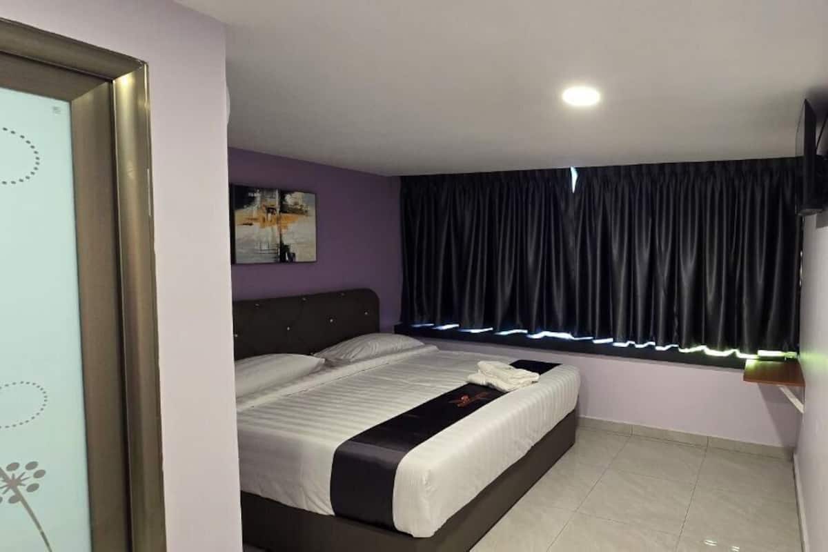 Ein Schlafzimmer mit einem Bett, einem Fenster mit Vorhängen, einem an der Wand befestigten Fernseher und einer Tür mit Fensterteil.
