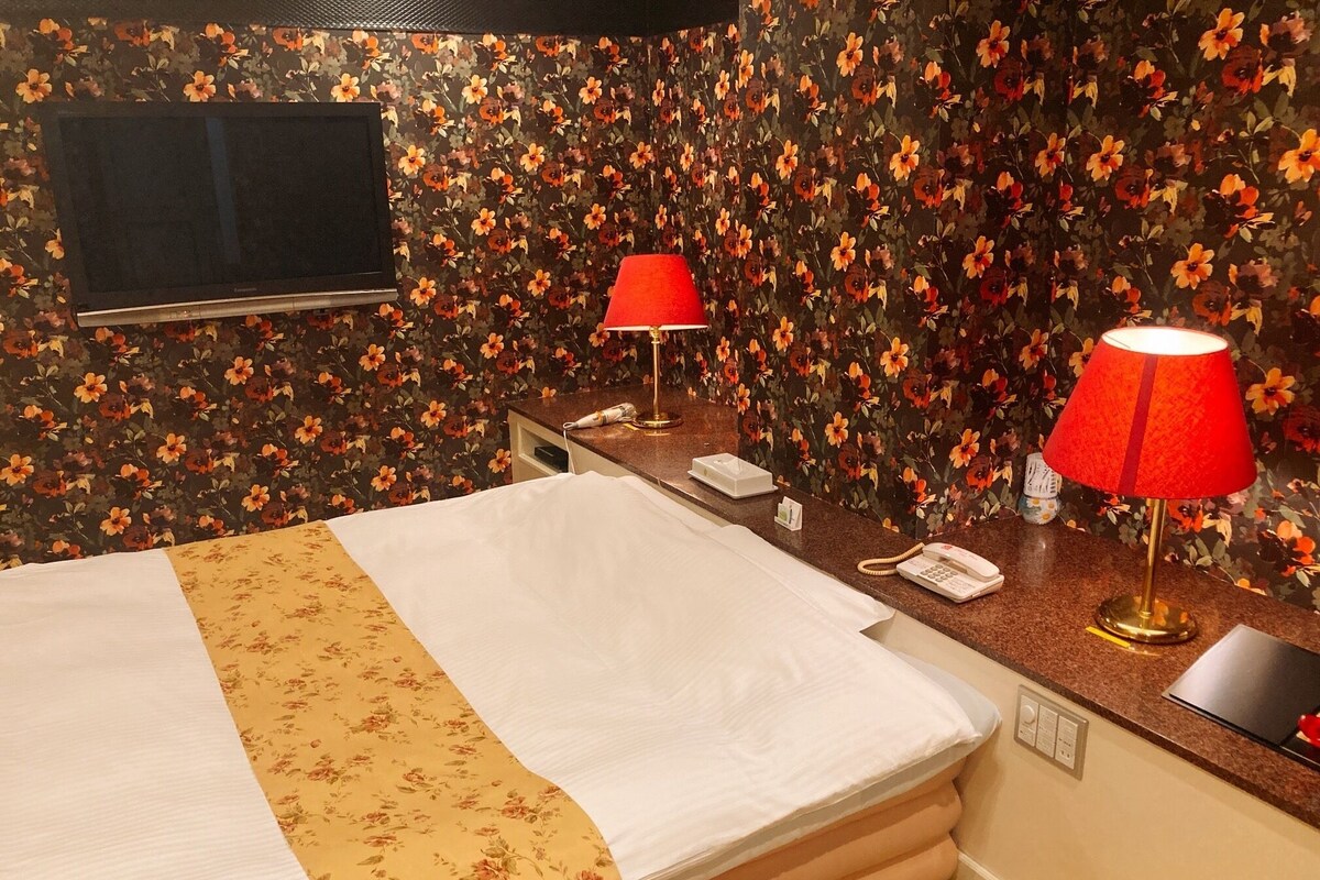 Une chambre d’hôtel équipée d’un lit, d’un bureau avec un téléphone et une lampe, et d’un téléviseur fixé au mur.