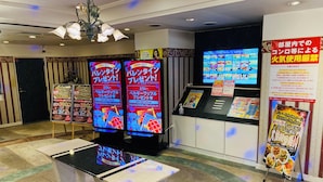 Een hotel lobby met een receptiebalie, twee digitale schermen die promotie-inhoud tonen, een kroonluchter en een behang met een patroon.