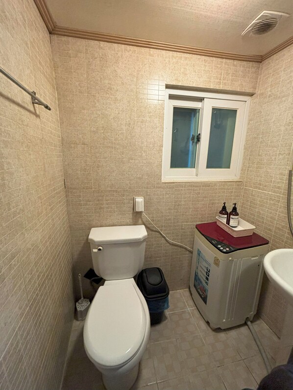 A small bathroom with a toilet, a washing machine, and a window. - Sunrise Inn (Seoul)