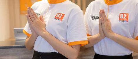 Deux personnes vêtues d’uniformes blancs et orange, ornés du logo « B2 », se tiennent debout, les mains jointes.