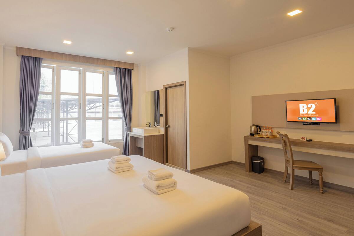 A hotel room with two beds, a desk, a TV, and a view of the outdoors.