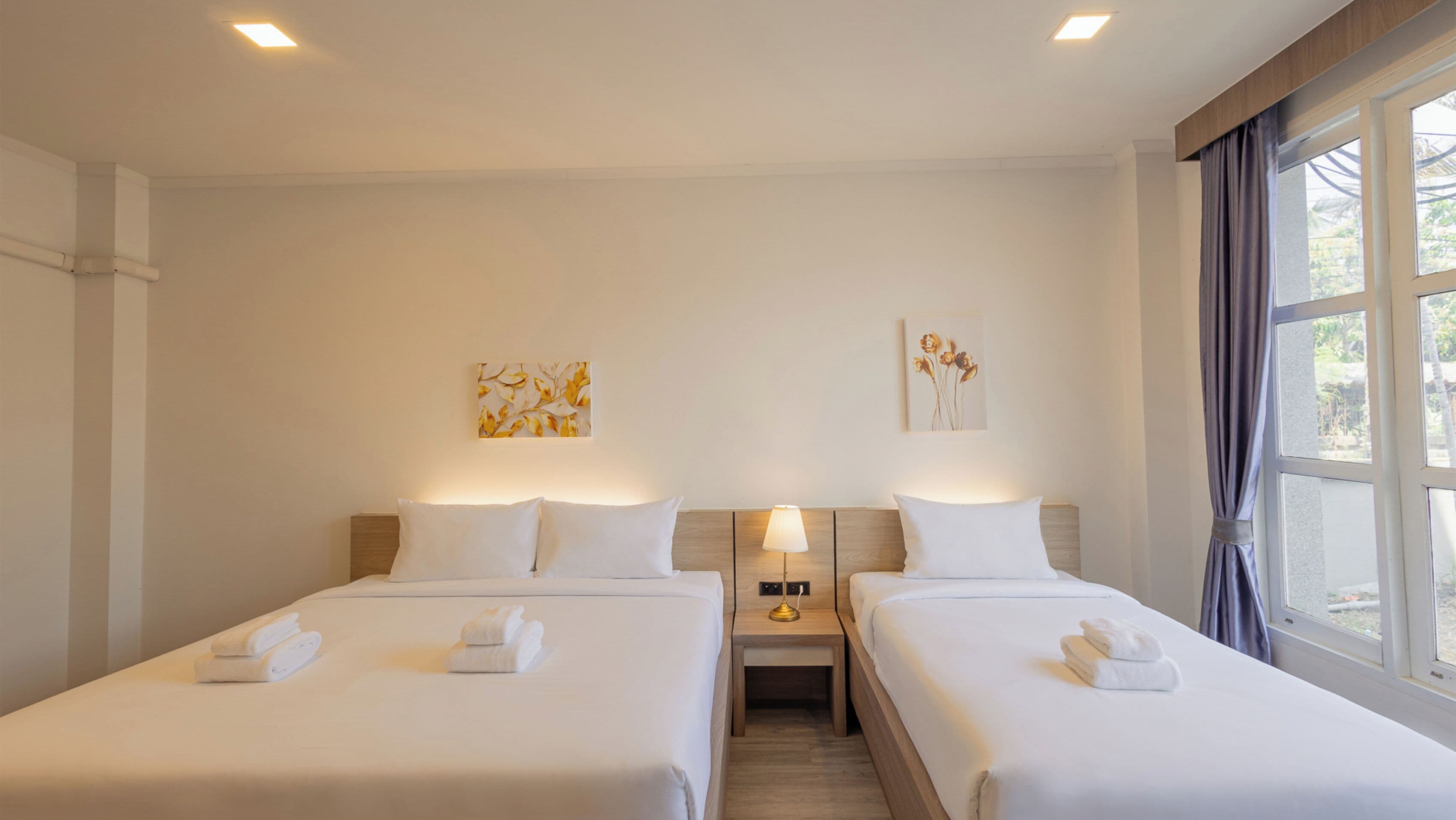 A hotel room with two beds, a nightstand with a lamp, and artwork on the walls.