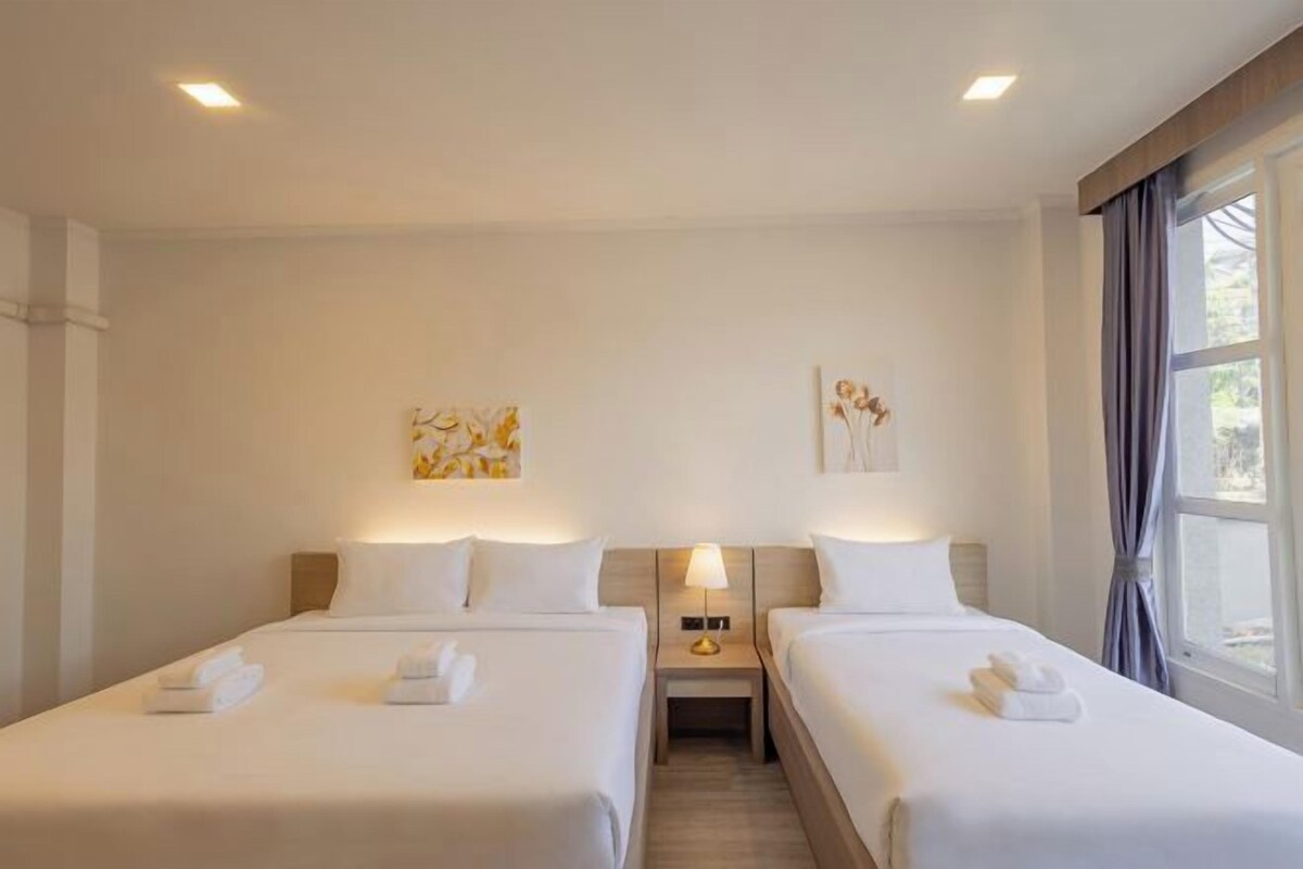 A hotel room with two beds, each with a nightstand, a lamp, and towels.