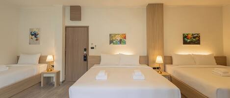A hotel room with two single beds and a larger bed, all neatly made with white linens and towels. There are small bedside tables with lamps, and the room has a wooden floor and walls.