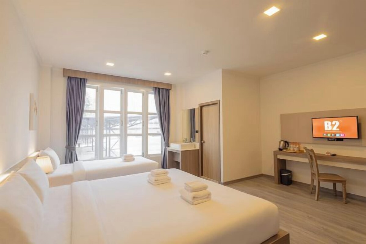 A hotel room with two beds, a desk, a TV, and a window with curtains.