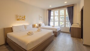 Habitación de hotel con dos camas, una ventana con cortinas, una mesita de noche con lámpara y un baño con lavamanos y espejo.