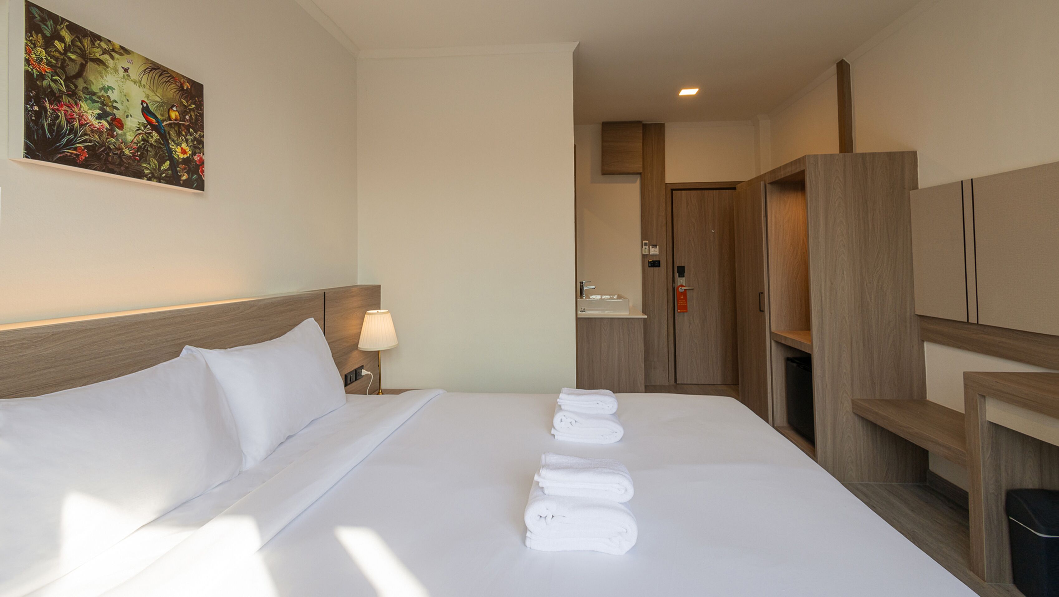 Ein Hotelzimmer mit einem ordentlich bezogenen Bett, einem Bild an der Wand und einem durchgegangenen Tür erkennbaren Badezimmer.