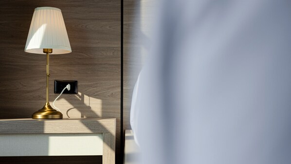 A bedside table with a lamp, a power outlet, and a wooden wall.