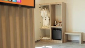 Habitación de hotel con un armario de madera, un banco, un refrigerador pequeño y un estante con artículos de aseo.