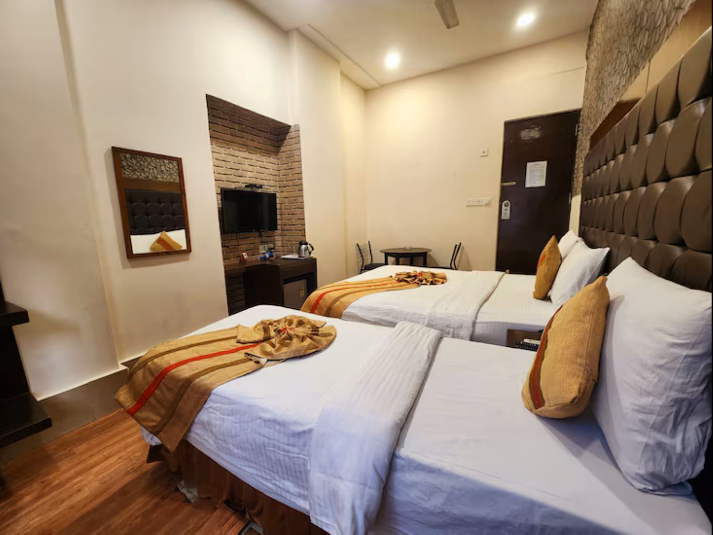 A hotel room with two beds, a television, a desk, and a brick accent wall.