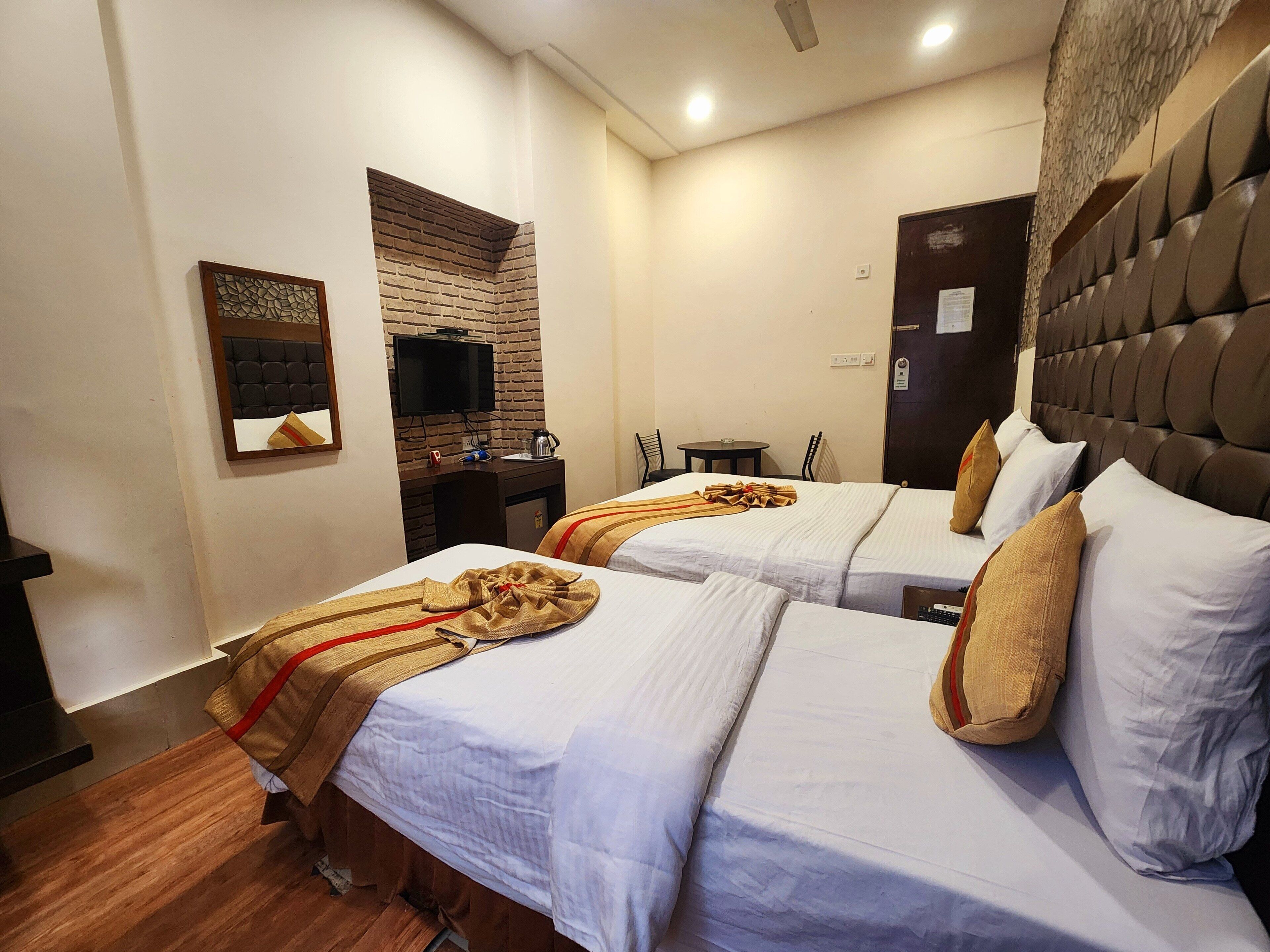 A hotel room with two beds, a TV, a small table, and a wall-mounted heater.