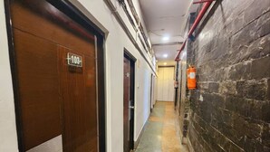 A narrow hallway with a wooden door labeled '103' and a fire extinguisher mounted on the wall. - HOTEL RAUNAK (Kolkata)