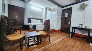 A hotel room with a bed, a wooden chair, a small table, a fan, and a kitchen area with a kettle. - HOTEL RAUNAK (Kolkata)