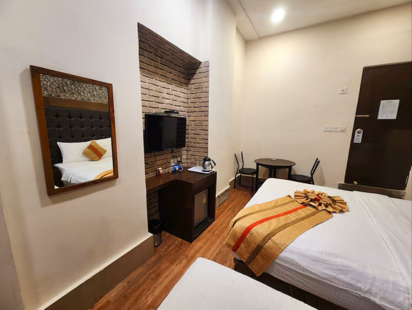A hotel room with a bed, a desk with a TV, a small table, and a chair.
