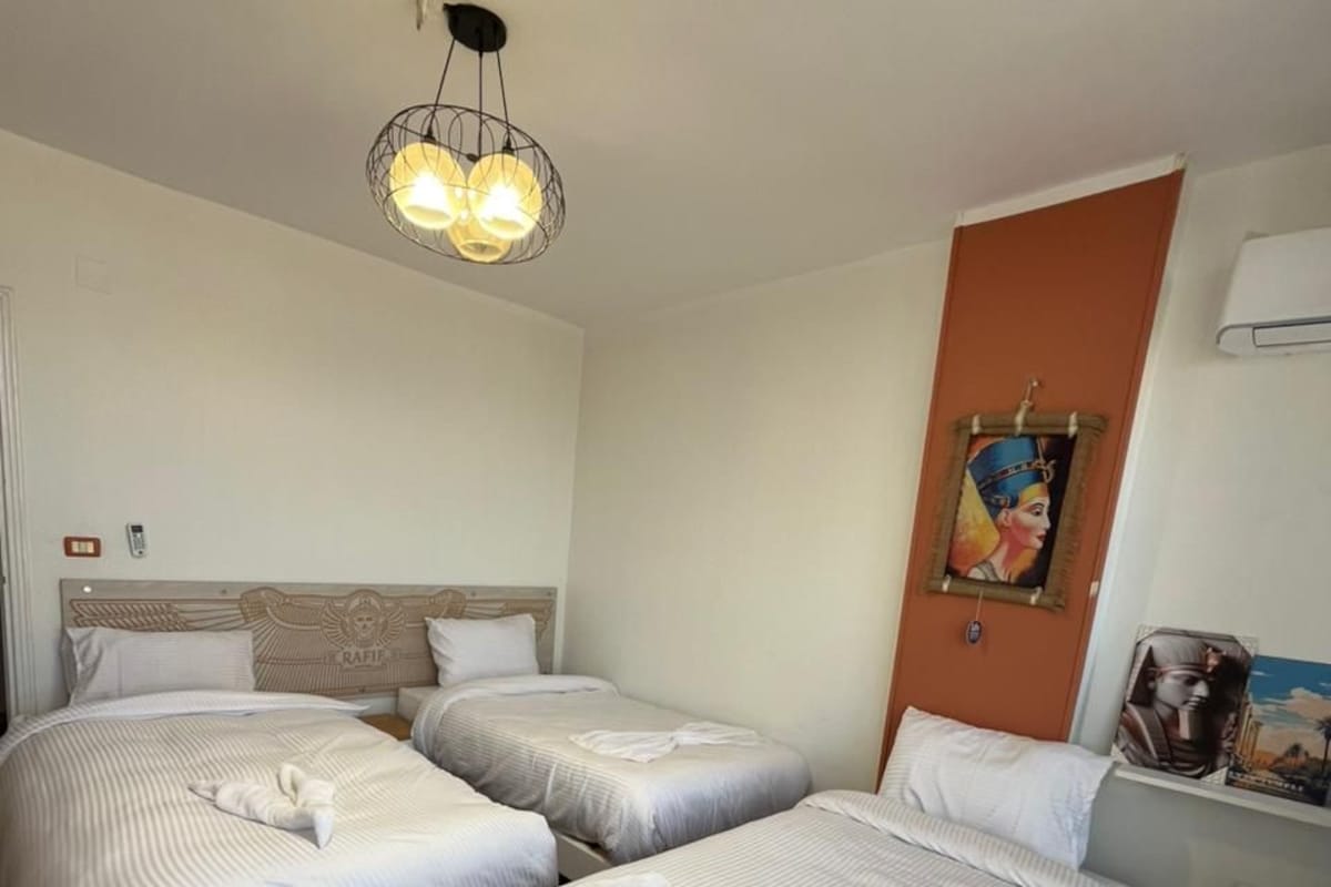 Habitación de hotel con dos camas, una mesita, un cuadro y una lámpara en el techo.