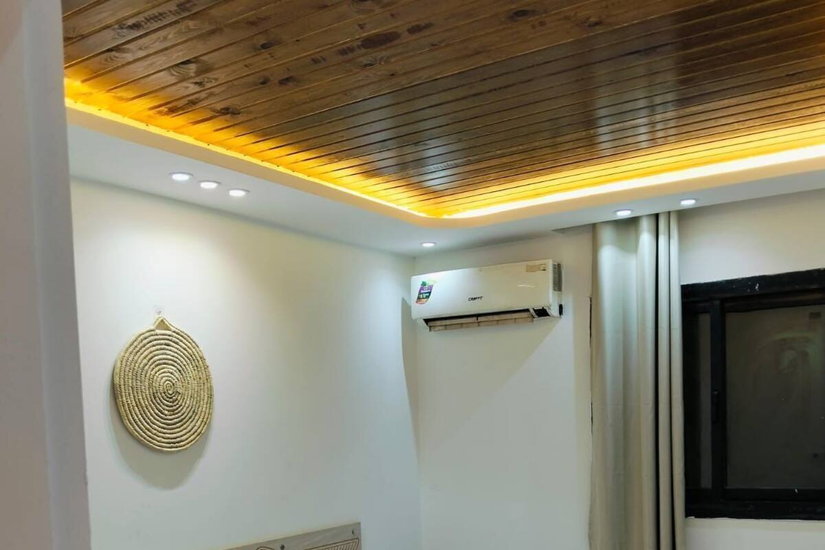 A hotel room with two single beds, a wooden ceiling, an air conditioning unit, and a window with curtains.